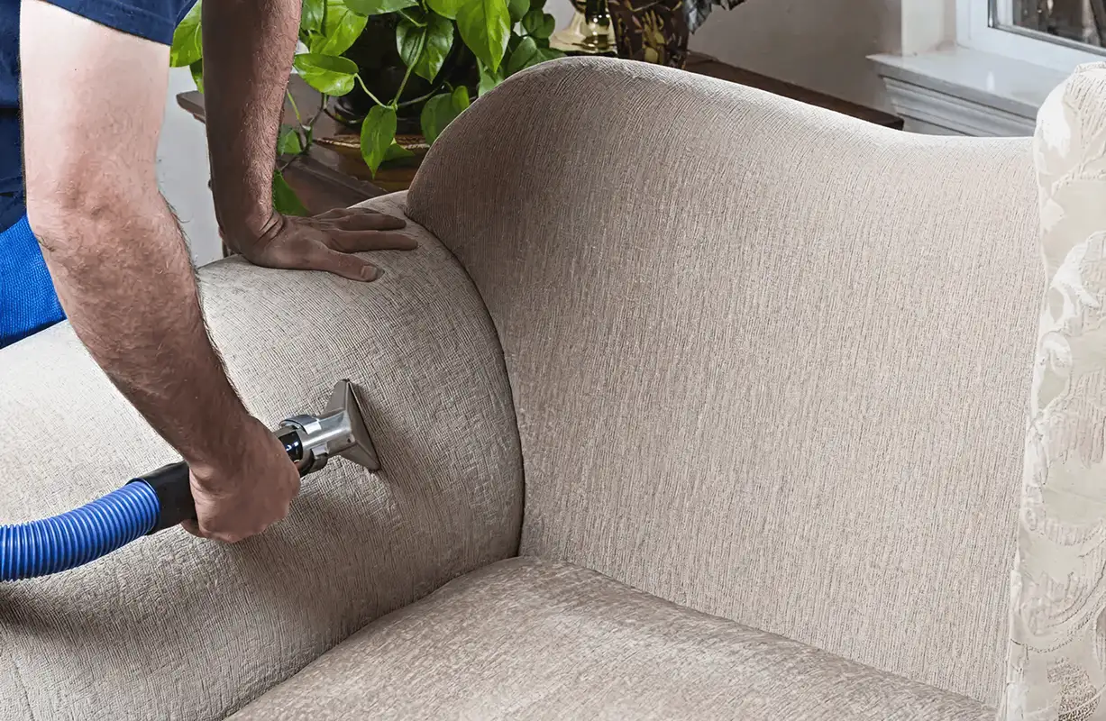 Professional upholstery cleaner deep-cleaning a fabric sofa with a handheld extraction tool and hose, Arlington, TX.